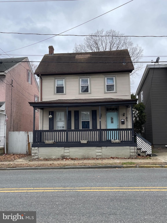 view of front facade with covered porch, a chimney, and fence