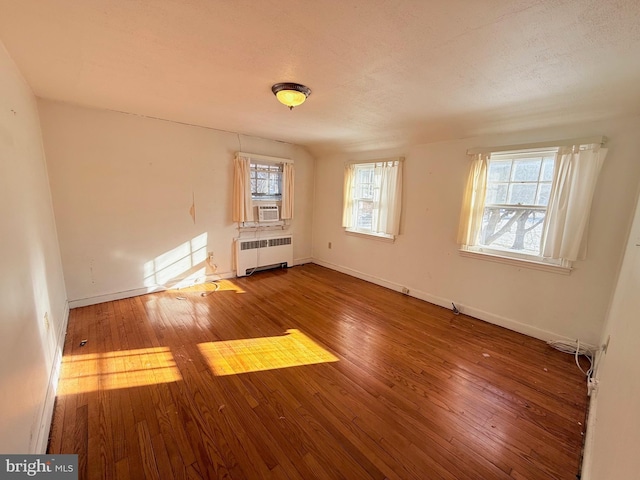 unfurnished room with radiator heating unit, cooling unit, and wood-type flooring