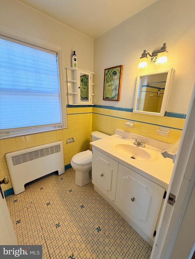 bathroom featuring radiator, tile patterned flooring, toilet, vanity, and tile walls