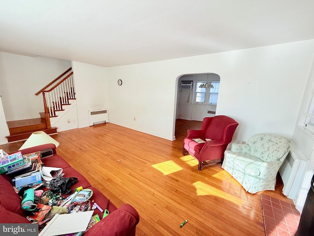 living room featuring a wall unit AC, radiator heating unit, hardwood / wood-style floors, and a notable chandelier