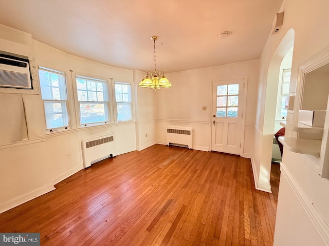 unfurnished dining area with an AC wall unit, light hardwood / wood-style flooring, radiator, and an inviting chandelier