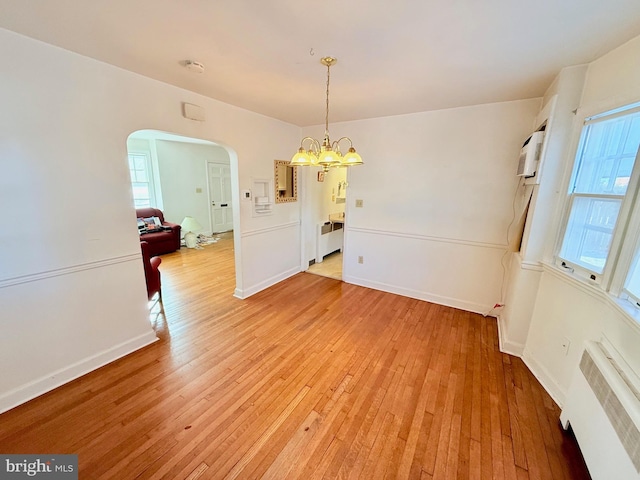 unfurnished dining area featuring light wood-type flooring, radiator, and a notable chandelier