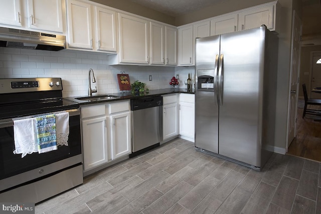 kitchen featuring white cabinetry, sink, range hood, decorative backsplash, and appliances with stainless steel finishes