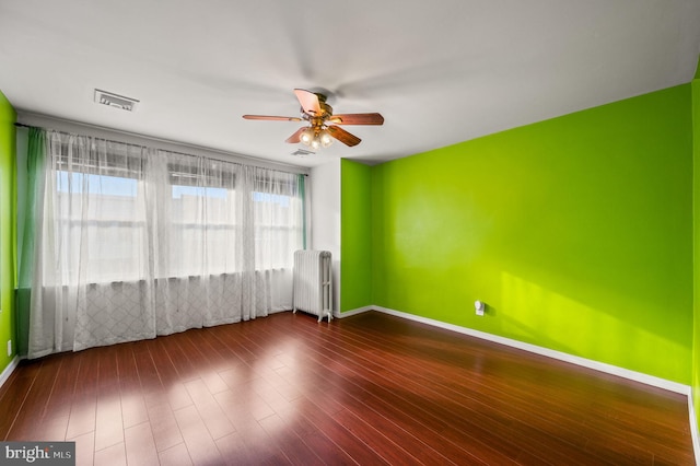 unfurnished room with plenty of natural light, dark hardwood / wood-style floors, radiator heating unit, and ceiling fan