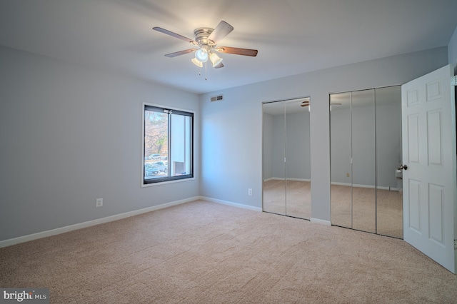 unfurnished bedroom with ceiling fan, light colored carpet, and multiple closets