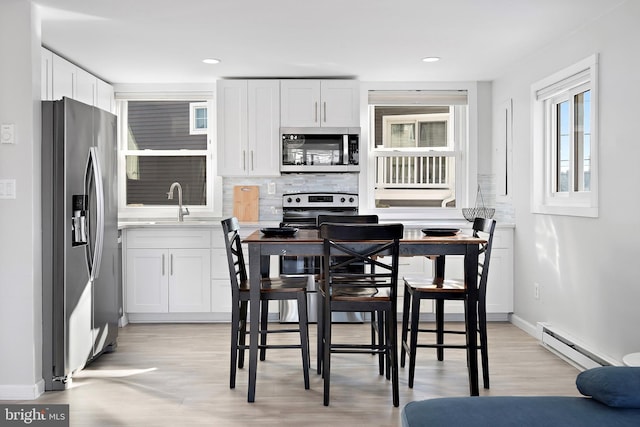 kitchen with decorative backsplash, white cabinets, stainless steel appliances, and a baseboard radiator