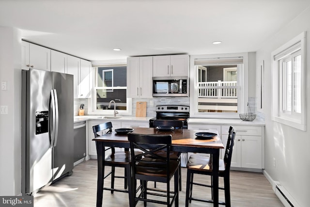 kitchen featuring appliances with stainless steel finishes, backsplash, baseboard heating, sink, and white cabinetry