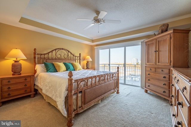 carpeted bedroom featuring access to exterior, ceiling fan, a textured ceiling, a tray ceiling, and ornamental molding