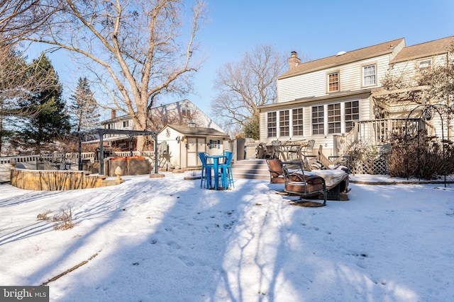 snow covered house with a storage unit, a deck, and an outdoor fire pit