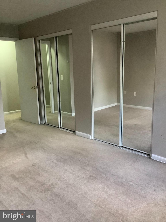 unfurnished bedroom featuring light colored carpet and two closets