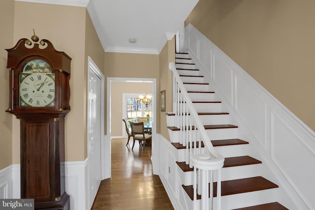 staircase featuring ornamental molding, wood-type flooring, and a notable chandelier