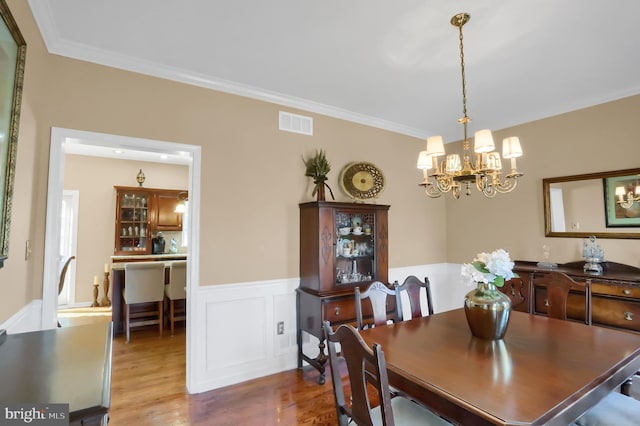 dining space featuring wood-type flooring, ornamental molding, and an inviting chandelier