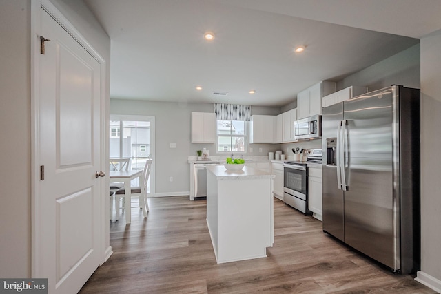 kitchen featuring white cabinets, stainless steel appliances, light wood-type flooring, and a kitchen island