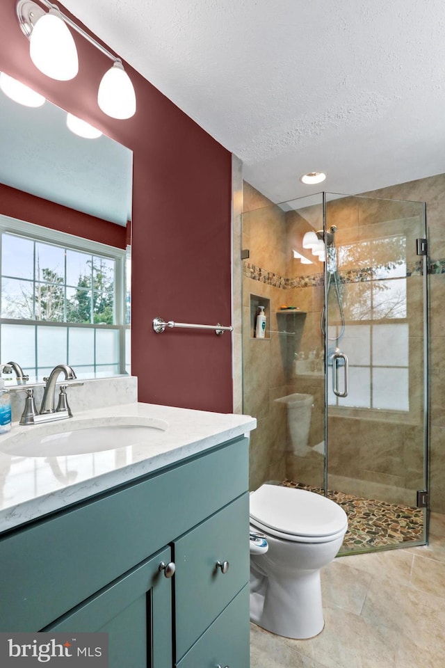 bathroom with a textured ceiling, tile patterned floors, vanity, toilet, and walk in shower