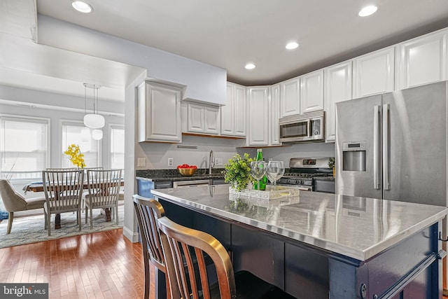 kitchen with stainless steel appliances, decorative light fixtures, white cabinetry, dark stone counters, and dark wood-type flooring