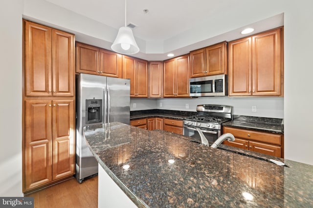 kitchen with decorative light fixtures, sink, light wood-type flooring, appliances with stainless steel finishes, and dark stone counters