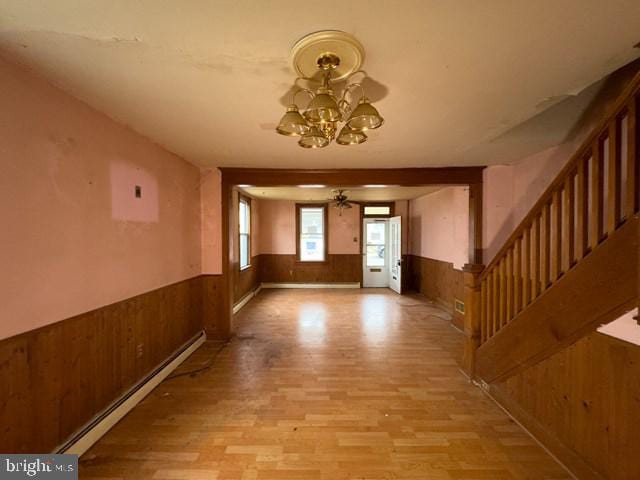 entrance foyer with ceiling fan with notable chandelier, light hardwood / wood-style flooring, wooden walls, and a baseboard radiator