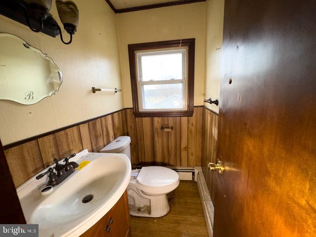 bathroom featuring baseboard heating, crown molding, toilet, vanity, and hardwood / wood-style flooring