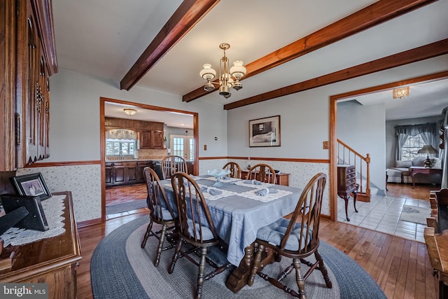 dining space featuring beam ceiling, light hardwood / wood-style floors, and an inviting chandelier