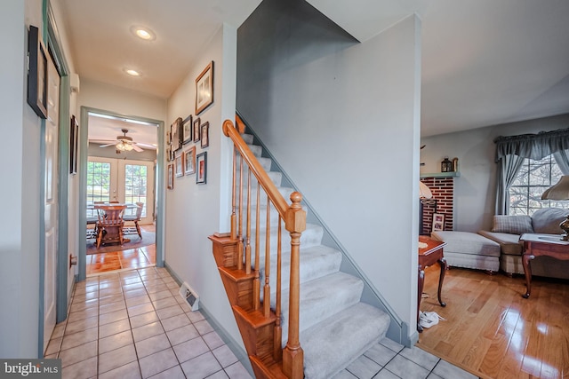 stairway featuring tile patterned flooring, ceiling fan, and a fireplace