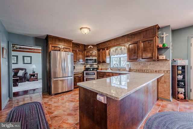 kitchen featuring light stone countertops, appliances with stainless steel finishes, backsplash, kitchen peninsula, and sink