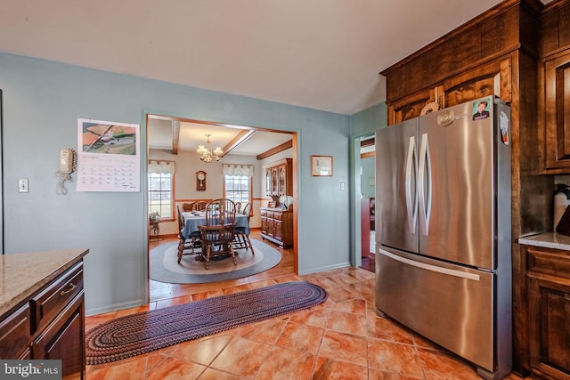 kitchen featuring stainless steel fridge, light tile patterned floors, a notable chandelier, light stone counters, and dark brown cabinets