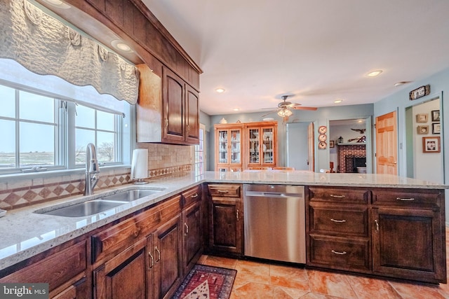 kitchen featuring dishwasher, backsplash, sink, light stone counters, and kitchen peninsula