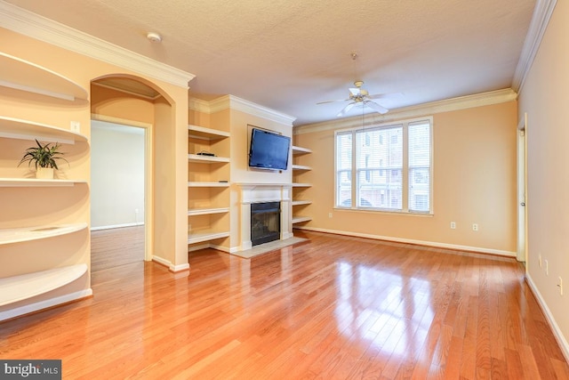 unfurnished living room with ceiling fan, crown molding, wood-type flooring, and built in features