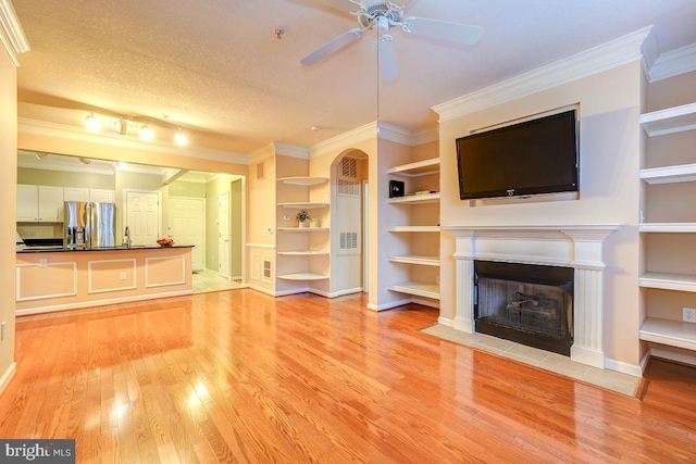 unfurnished living room with built in shelves, ceiling fan, crown molding, and light hardwood / wood-style flooring