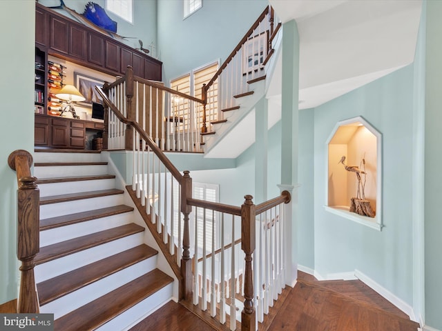 staircase featuring a towering ceiling and wood-type flooring