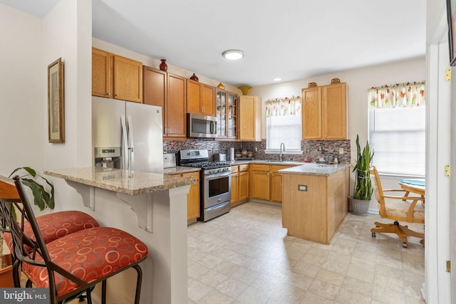 kitchen with kitchen peninsula, appliances with stainless steel finishes, a kitchen bar, and light stone countertops