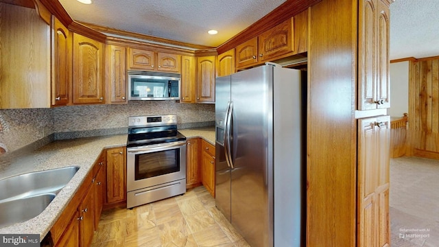 kitchen featuring a textured ceiling, appliances with stainless steel finishes, a sink, and brown cabinets