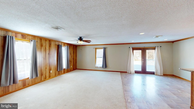 empty room featuring wood walls, visible vents, baseboards, french doors, and crown molding