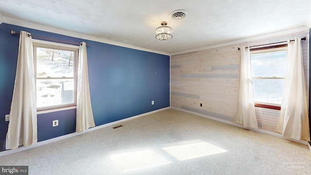 carpeted empty room with baseboards, wooden walls, visible vents, and crown molding