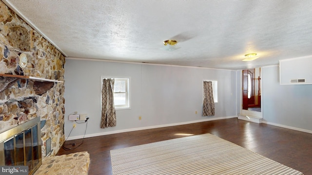 unfurnished living room with a textured ceiling, a stone fireplace, dark wood-style flooring, and visible vents