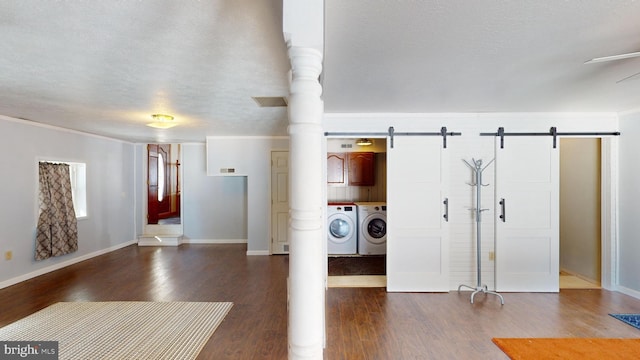 interior space with a textured ceiling, a barn door, dark wood-type flooring, baseboards, and washing machine and clothes dryer