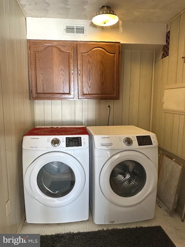 washroom featuring cabinet space, washing machine and dryer, wooden walls, and visible vents