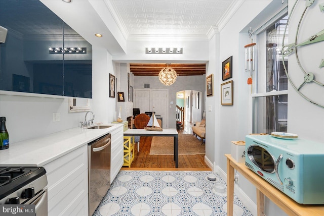 kitchen featuring stainless steel appliances, ornamental molding, a notable chandelier, sink, and white cabinetry