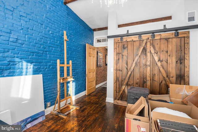 unfurnished room featuring brick wall, dark wood-type flooring, a barn door, and vaulted ceiling with beams