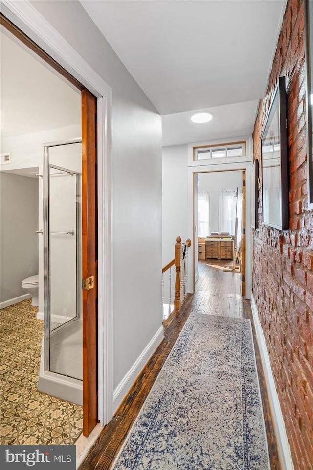 corridor with brick wall and wood-type flooring