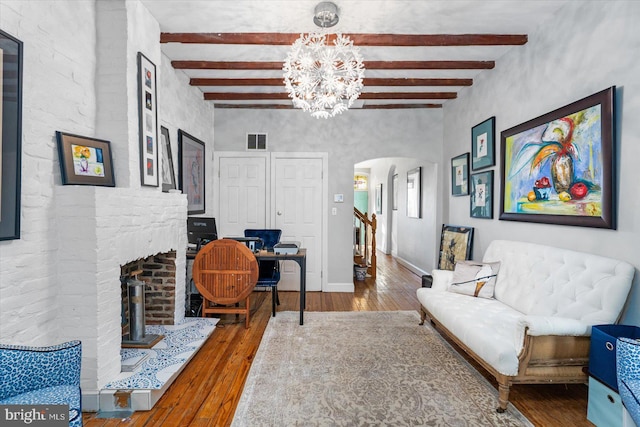 living room featuring a brick fireplace, an inviting chandelier, beamed ceiling, and hardwood / wood-style floors