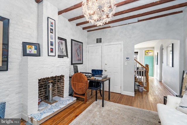 interior space with hardwood / wood-style floors, an inviting chandelier, beamed ceiling, and a fireplace