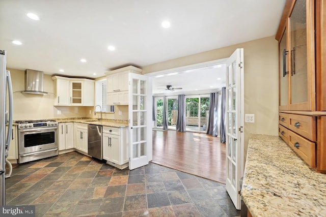 kitchen featuring appliances with stainless steel finishes, french doors, light stone countertops, white cabinets, and wall chimney range hood