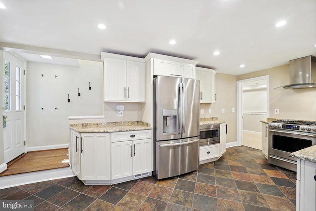 kitchen with stainless steel appliances, wall chimney exhaust hood, white cabinets, and light stone countertops