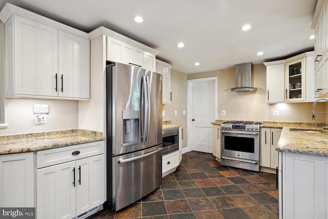 kitchen with white cabinets, wall chimney range hood, stainless steel appliances, sink, and light stone counters