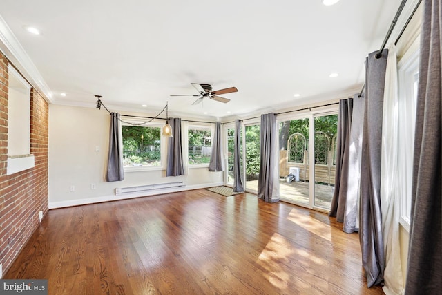 unfurnished room with baseboard heating, a wealth of natural light, ornamental molding, and hardwood / wood-style floors