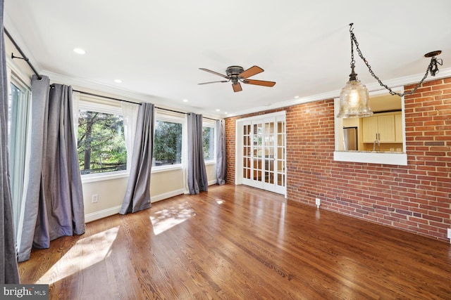 unfurnished living room with ceiling fan, brick wall, ornamental molding, and hardwood / wood-style floors