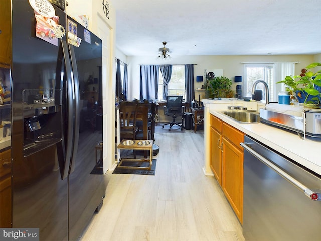 kitchen featuring brown cabinetry, dishwasher, black fridge with ice dispenser, light countertops, and a sink