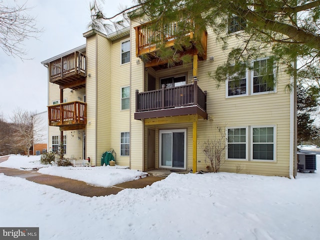 snow covered house featuring a balcony and central AC unit