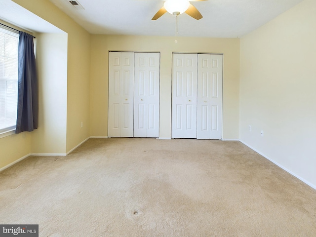 unfurnished bedroom featuring two closets, visible vents, light carpet, ceiling fan, and baseboards